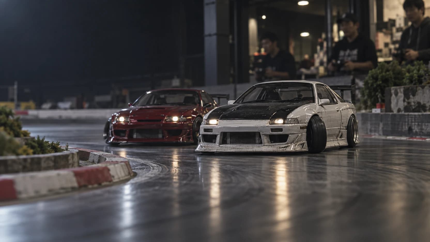 Two detailed scale RC drift cars holding a close tandem line on an indoor circuit.